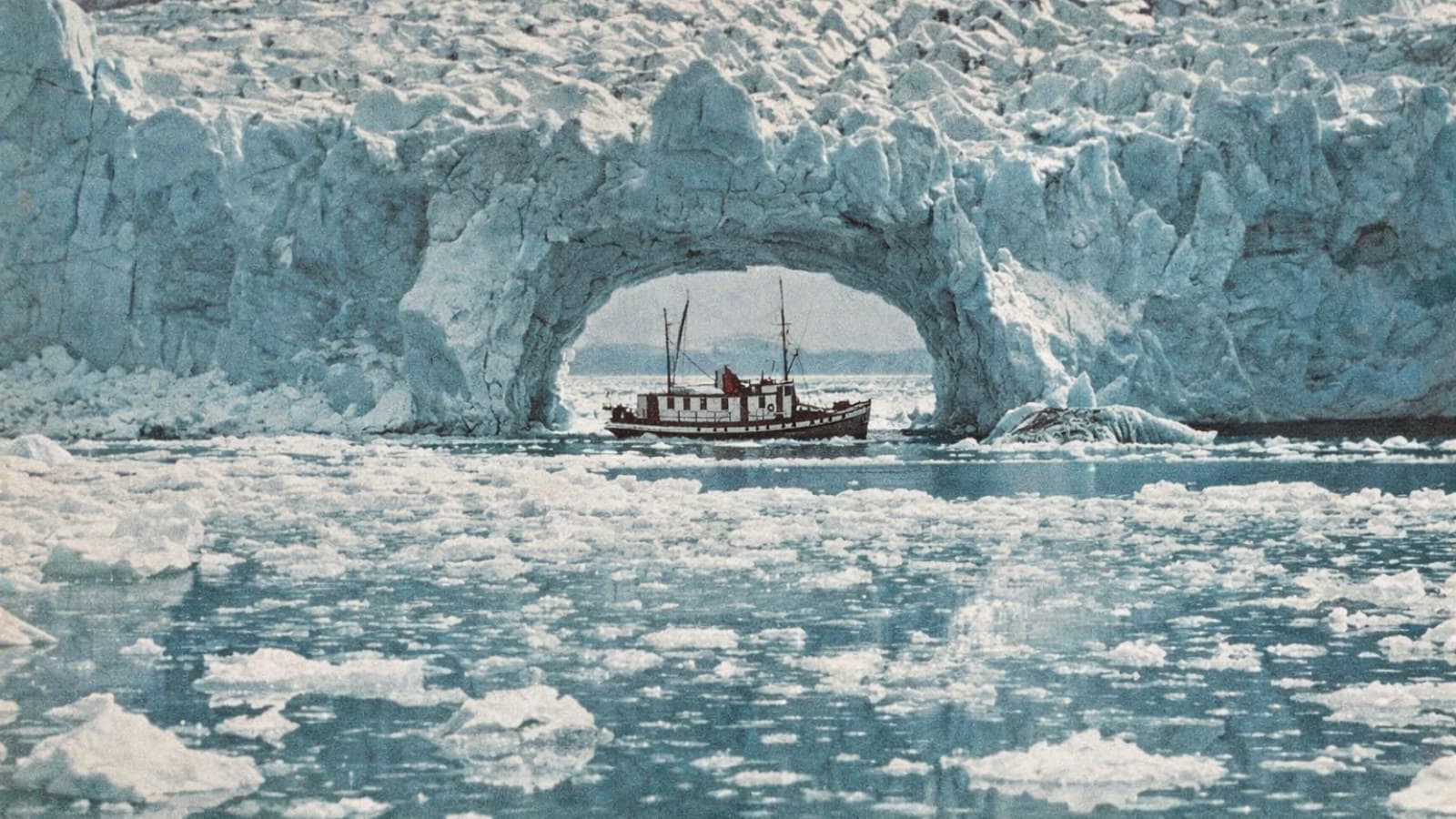 A working boat passing under a glacier arch through broken pack ice.